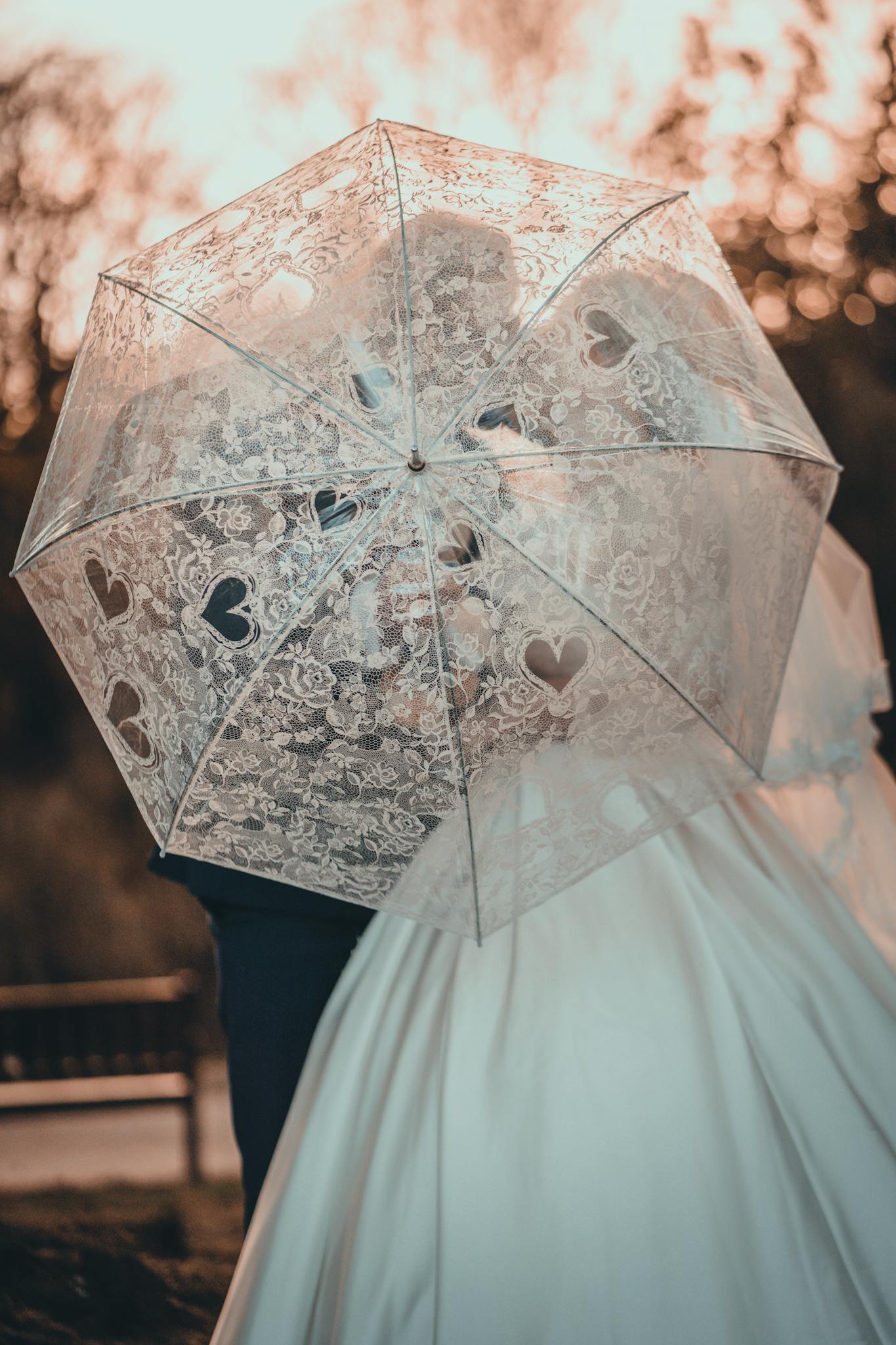 Romantic wedding couple sharing a moment under a lace umbrella at sunset.